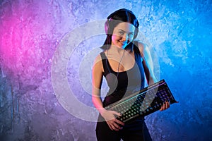 Young Disco Girl Wearing Gaming Headset Holding Gaming Kyeboard. Room Lit in Retro, Retrowave or Cyberpunk Style