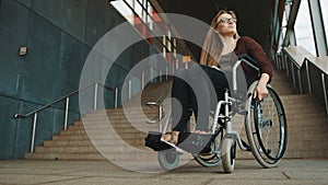 Young discouraged caucasian woman in the wheelchair in front of the staircase looking around for accessible way