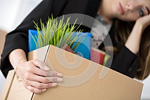 Young dismissed female worker in office holding carton box with