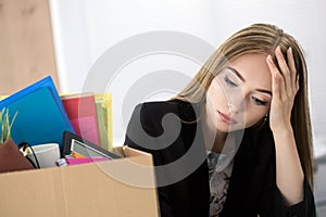 Young dismissed female worker in office sitting near carton box