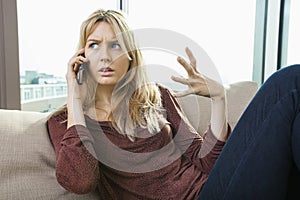 Young displeased woman talking on mobile phone at home