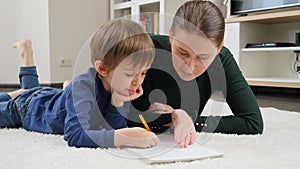 Young displeases mother shouting and talking strictly to her son doing homework on carpet at living room. Concept of