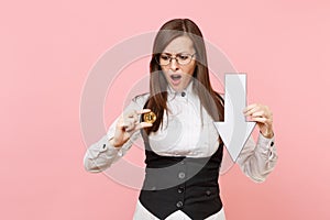 Young dissatisfied business woman in glasses holding bitcoin and down value fall arrow on pastel pink