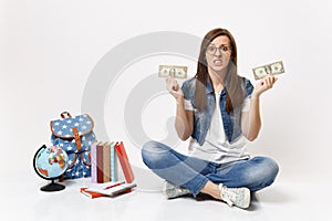 Young dissatisfied woman student hold dollar bills cash money feeling stressed by lack of money sit near globe backpack