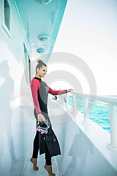 Young diver girl in black wetsuit standing on board of the yacht