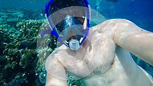 young diver wearing an underwater mask takes a selfie at the bottom of the blue sea