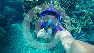 young diver wearing an underwater mask takes a selfie at the bottom of the blue sea