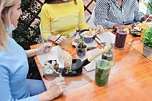 Young diverse friends having breakfast outdoors in restaurant terrace - Focus on center girl hands