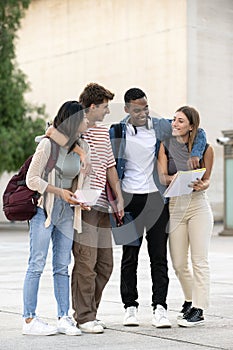 Young diverse friends walking together in embrace while reading notebooks. Joyful multiracial group of students walking