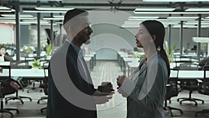 Young diverse man and woman colleagues talking together during coffee break, laughing at office, zoom in, side view