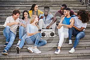 Young diverse people having fun listening music with boombox stereo outdoor in the city - Focus center african girl face