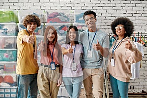 Young and diverse volunteer group smiling at camera, showing thumbs up while posing in front of boxes full of clothes