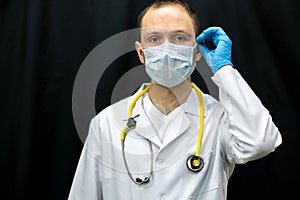 A young doctor in blue gloves and a stethoscope around his neck on a black background. Portrait of a doctor with medical