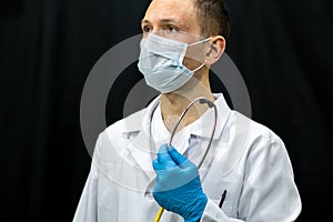 A young doctor in blue gloves and a stethoscope around his neck on a black background. Portrait of a doctor with medical