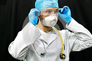 A young doctor in blue gloves and a stethoscope around his neck on a black background. Portrait of a doctor with medical