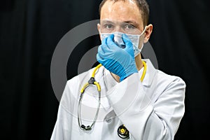 A young doctor in blue gloves and a stethoscope around his neck on a black background. Portrait of a doctor with medical