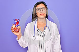 Young doctor cardiology specialist woman holding medical heart over pruple background with a confident expression on smart face