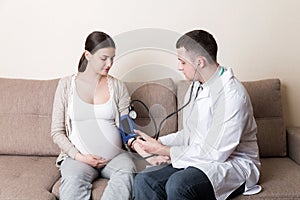 Young doctor is checking blood pressure of pregnant woman at home. High pressure problem during pregnancy concept