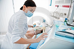 Young doctor checking breathing machine while putting oxygen mask on patient