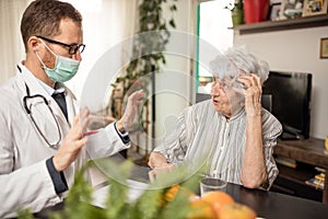 Young doctor consulting and advising senior woman during house call visit