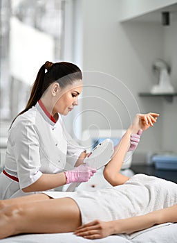 Young doctor cosmetician performs a cosmetic procedure on the patient`s hand with electronic medical equipment in beauty parlor