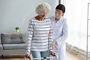 Young doctor helping older disabled patient walking with frame.