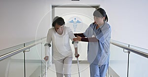 Young doctor helping patient use crutches in hospital 4k