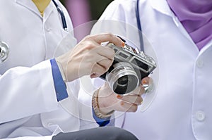 Young doctor with hijab sitting on bench at park and holding vintage camera