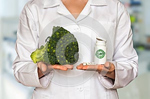 Young doctor holding fresh broccoli and bottle of pills with vit