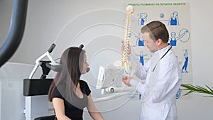 Young doctor holding spine model near patient in hospital.