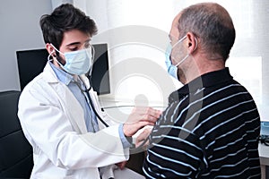Young doctor listening to mature man patient heart and lungs with a stethoscope