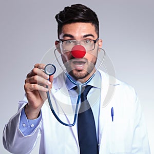 Young doctor listens to you at stethoscope with red nose