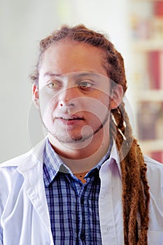 Young doctor with long dread locks posing for camera, clinic in background, medical concept