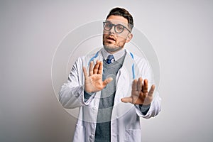 Young doctor man with blue eyes wearing medical coat and stethoscope over isolated background Moving away hands palms showing