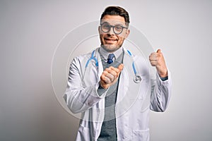 Young doctor man with blue eyes wearing medical coat and stethoscope over isolated background Pointing to the back behind with