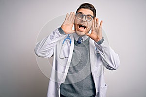 Young doctor man with blue eyes wearing medical coat and stethoscope over isolated background Smiling cheerful playing peek a boo