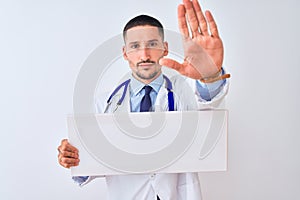 Young doctor man holding blank advertising banner over isolated background with open hand doing stop sign with serious and