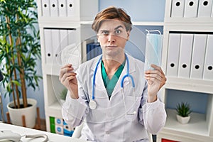 Young doctor man holding two safety mask skeptic and nervous, frowning upset because of problem