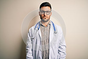 Young doctor man wearing glasses, medical white robe and stethoscope over isolated background depressed and worry for distress,