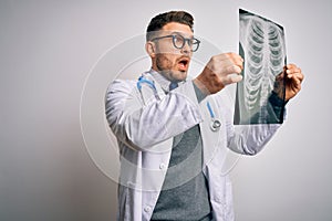 Young doctor man wearing medical coat looking at chest scan radiography over isolated background scared in shock with a surprise