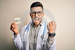 Young doctor man wearing stethoscope holding help note over isolated background annoyed and frustrated shouting with anger, crazy