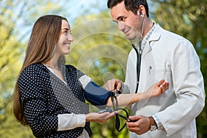 Young doctor measuring pressure to young lady in the park.