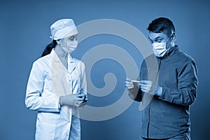 Young doctor measuring temperature of a patient with thermometer, studio shot on blue background