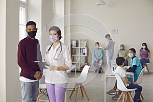 Nurse and patient in face masks standing in hospital office during vaccination campaign