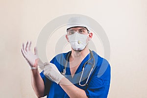 Young doctor portrait in protective breathing mask puts gloves on his hands isolated