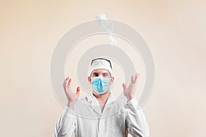 Young doctor portrait in protective breathing mask throws down white gloves on yellow background isolated