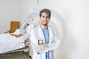 Young doctor posing in corporate portrait with sick patient lying in bed