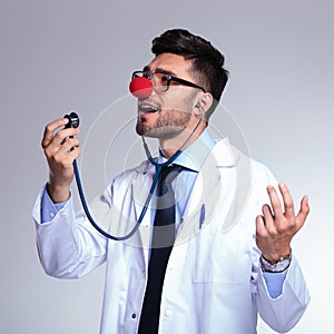 Young doctor with red nose singing in the stethoscope