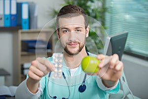 Young doctor showing apple and tablets