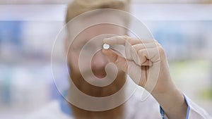 Young doctor shows a white round pill and nods his head approvingly